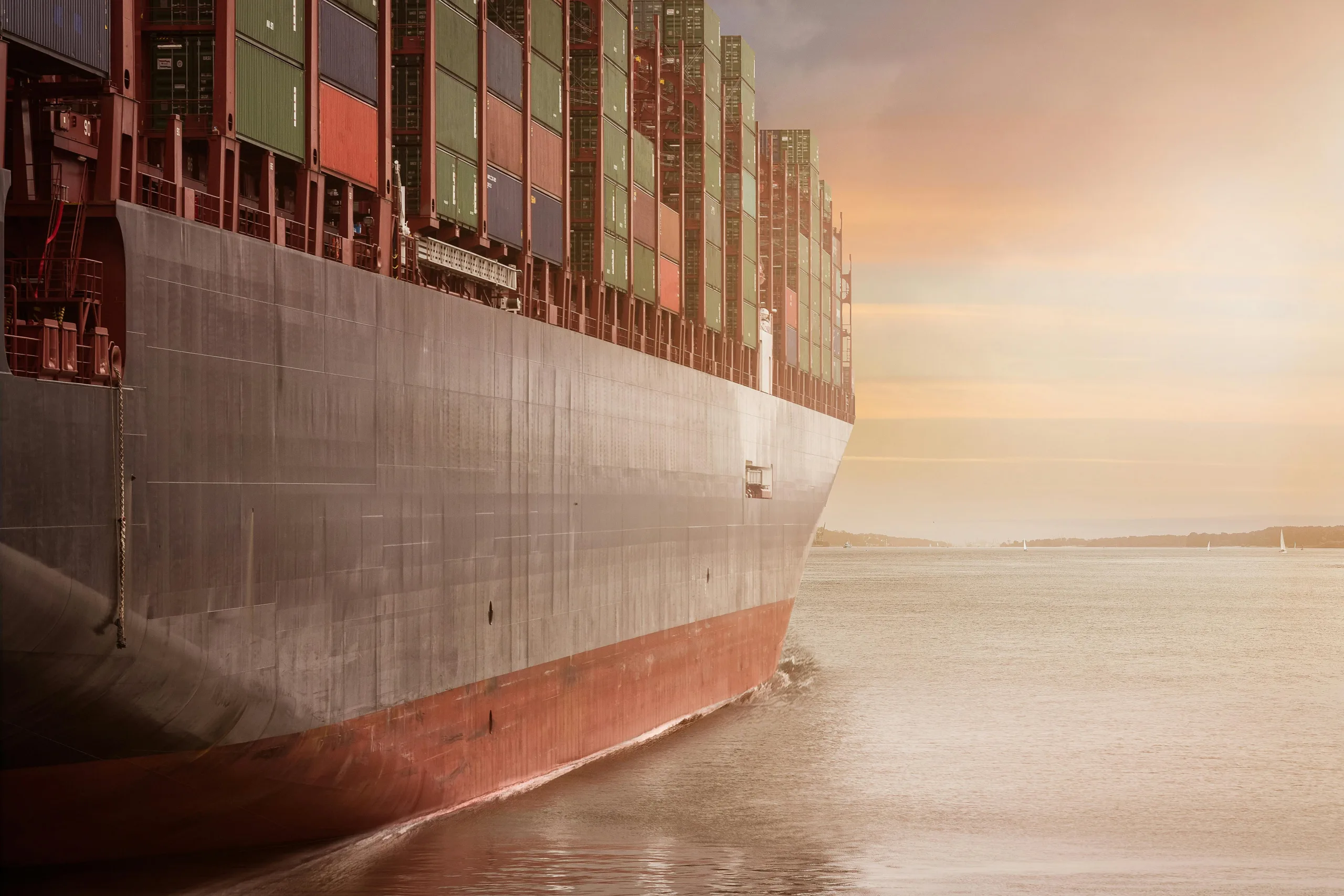 Service de Dropshipping 8 A colossal cargo ship loaded with containers navigates through calm waters against a vibrant sunset sky.