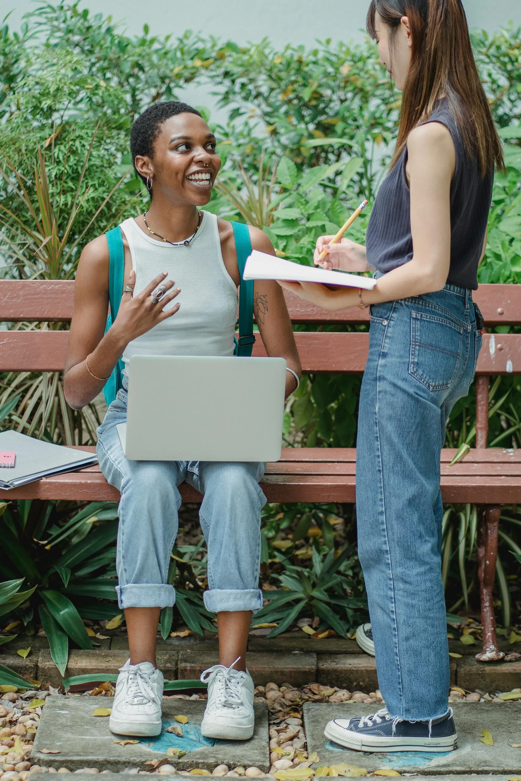 الخدمة الإضافية 2 Full body multiracial female friends talking with each other outside while studying on netbook and using notebook while looking at each other