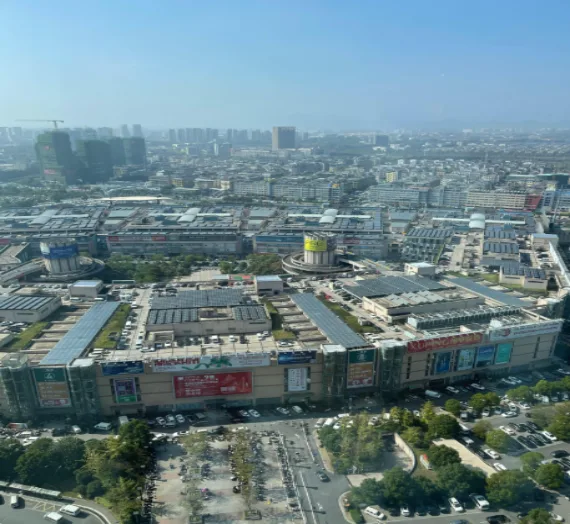 A high-angle photo showing a sprawling urban commercial area with shopping centers, roads, and dense city buildings under a clear blue sky.