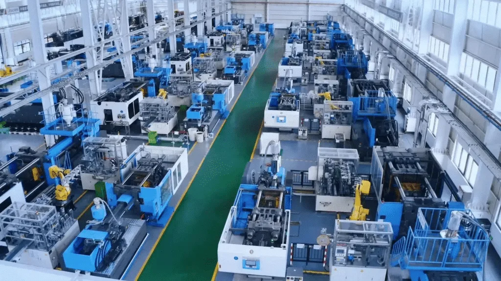 Interior view of a modern plastic injection molding factory with multiple automated molding machines arranged in rows along a central walkway.